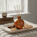 Cinnamon and clove reed diffuser in amber glass bottle with natural rattan reeds on wooden tray