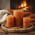 Set of 3 amber and terracotta pillar candles on wooden tray with dried leaves and cinnamon sticks